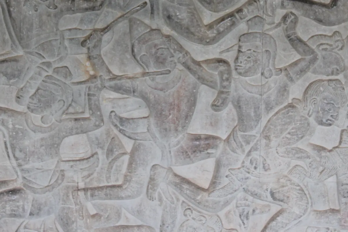 A weathered stone bas-relief at Angkor Wat showing carved figures, one with a bent arm raised in an elbow strike.
