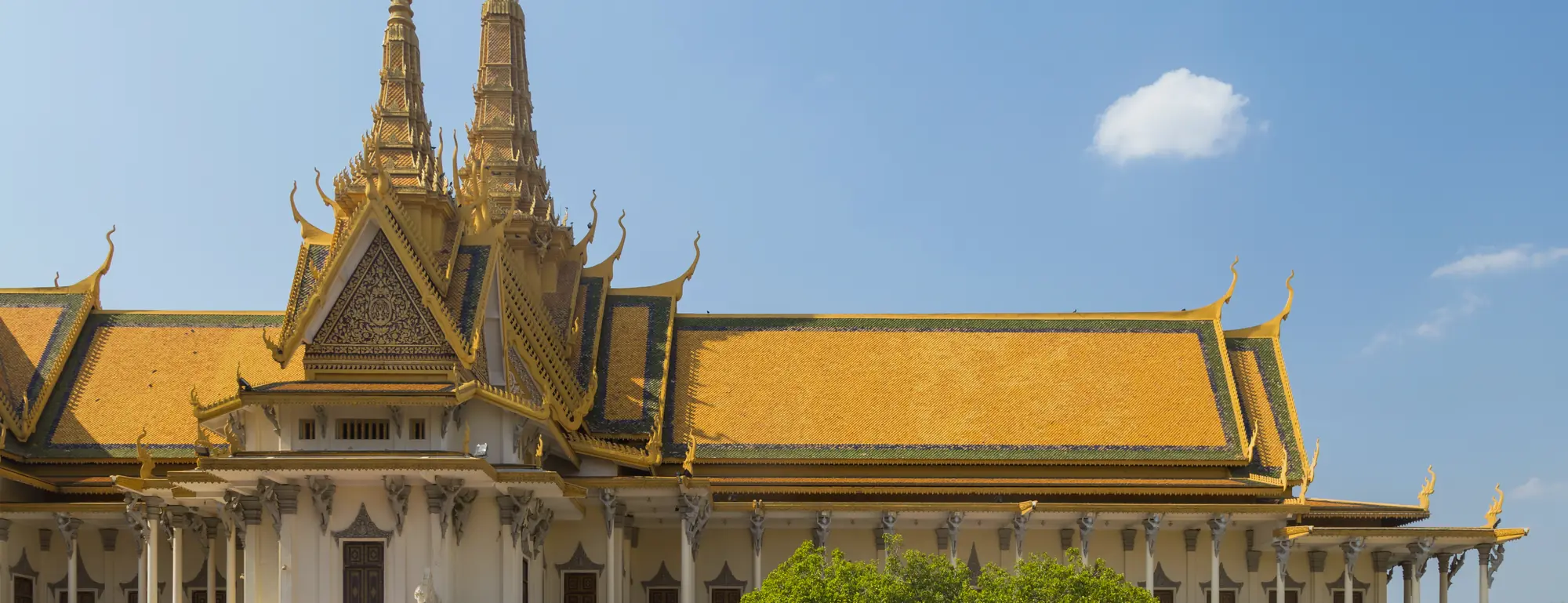 The golden-roofed Throne Hall of the Royal Palace in Phnom Penh, with two tall spires and white columns under a blue sky.